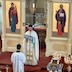 Fr. Aleksey is standing in front of the Royal Doors, holding the Royal Gifts and facing away from the altar. There's an altar server standing in front of the priest and facing him; the server's back is facing the camera. Both are wearing white vestmenets, and the Royal Gifts are covered with a light-blue cloth. There's also a light-blue cloth draped over the priest's left forearm.