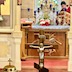 A gold cross is shown in the bottom center of the frame and is the focus of the photo. In the background, Fr. Aleksey is seen, through the Royal Doors, standing behind the altar with his head bowed.