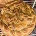 A close-up of a completed paska loaf with two large braids criss-crossing the loaf and an s-shape in each of the quadrants created by the criss-cross. The round loaf has another braid around the circumference of the loaf. The loaf is beautiful! Part of a second paska loaf is visible in the upper left corner of the frame.
