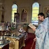 Fr. Aleksey is standing along the right side of the frame, wearing a light blue vestment and holding a praybook. He's facing left, where there's the center table and a large, silver vessel on a stand to the left of the table. In his right hand, Fr. Aleksey is holding a censor, which is only partly visible as it extends past the bottom of the frame.