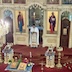Fr. Aleksey, wearing white vestments and facing the congregation, reads from the holy bible as he stands in the doorway of the Royal Doors.